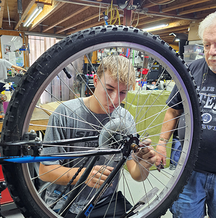 A man working on a bicycle wheel with another man.